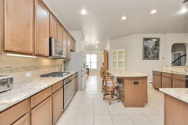 kitchen with a center island, light stone countertops, a breakfast bar area, and appliances with stainless steel finishes