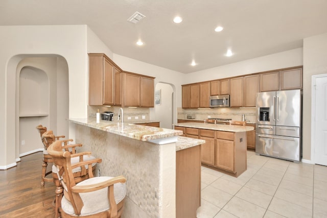 kitchen featuring light stone countertops, kitchen peninsula, decorative backsplash, light tile patterned floors, and appliances with stainless steel finishes