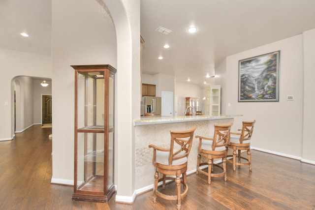 kitchen with kitchen peninsula, stainless steel refrigerator with ice dispenser, dark hardwood / wood-style flooring, and a kitchen breakfast bar