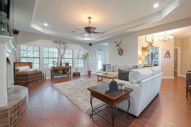 living room with a raised ceiling, ornamental molding, dark hardwood / wood-style floors, and ceiling fan with notable chandelier