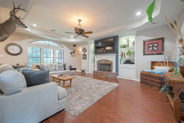 living room featuring built in features, ceiling fan, dark hardwood / wood-style flooring, a brick fireplace, and a raised ceiling