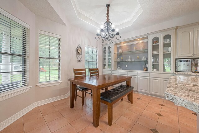 tiled dining space featuring ornamental molding, a raised ceiling, a textured ceiling, an inviting chandelier, and built in shelves