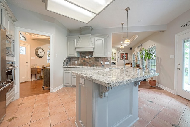 kitchen featuring a breakfast bar, an island with sink, sink, hanging light fixtures, and light tile patterned floors