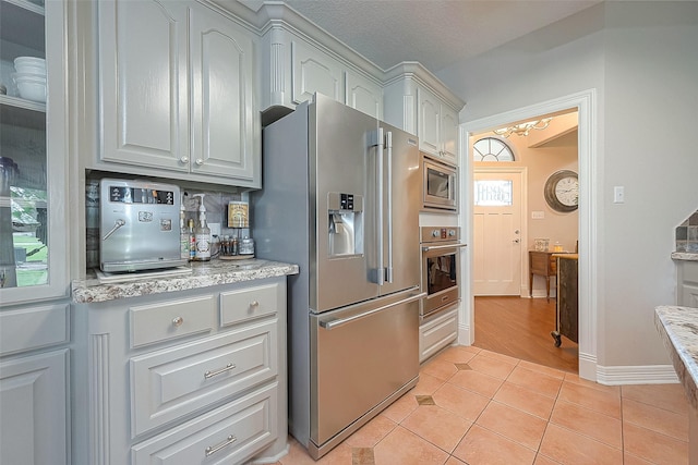 kitchen with stainless steel appliances, light tile patterned floors, a textured ceiling, and light stone counters