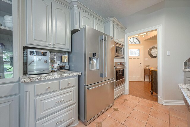 kitchen with stainless steel appliances, light tile patterned floors, a textured ceiling, and light stone counters