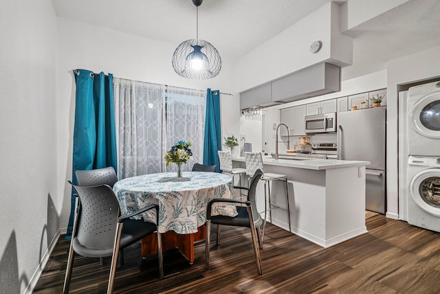 dining area featuring dark hardwood / wood-style flooring, stacked washer and clothes dryer, and sink