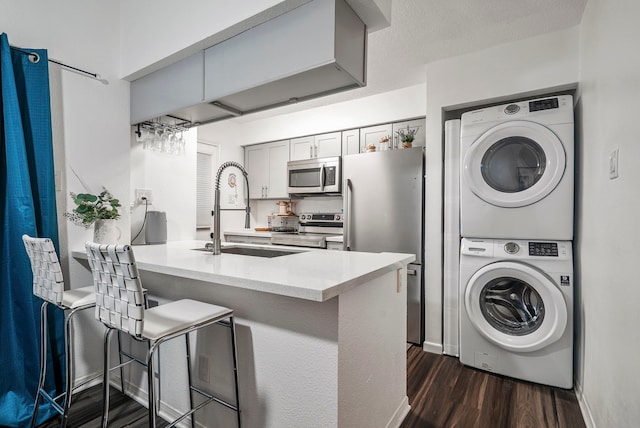 kitchen with kitchen peninsula, appliances with stainless steel finishes, a kitchen breakfast bar, stacked washing maching and dryer, and sink