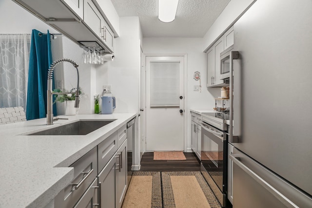 kitchen featuring sink, stainless steel appliances, light stone counters, a textured ceiling, and gray cabinets