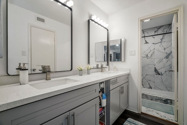 bathroom featuring hardwood / wood-style floors, vanity, a tile shower, and a textured ceiling