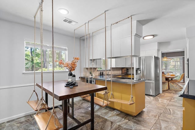 kitchen featuring kitchen peninsula, stainless steel fridge, backsplash, sink, and white cabinets