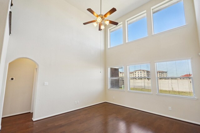 unfurnished room featuring ceiling fan, dark hardwood / wood-style flooring, and a towering ceiling