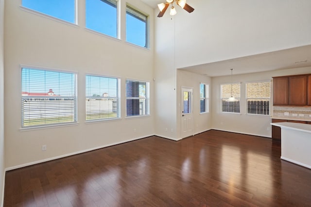 unfurnished living room with ceiling fan, a towering ceiling, and dark hardwood / wood-style floors