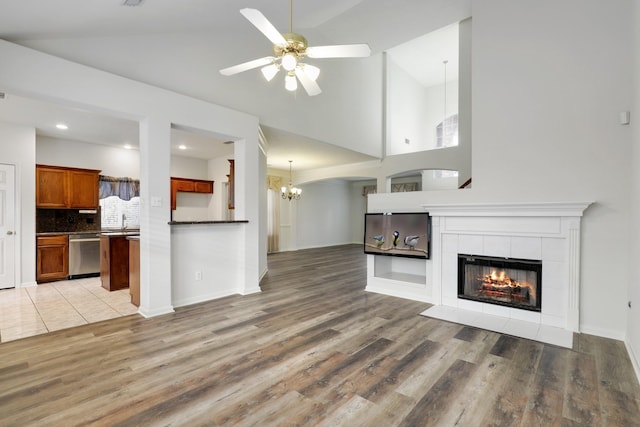 unfurnished living room featuring a towering ceiling, ceiling fan, sink, a tile fireplace, and hardwood / wood-style flooring