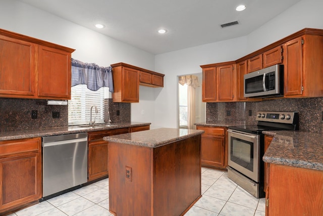 kitchen featuring appliances with stainless steel finishes, dark stone counters, sink, a kitchen island, and light tile patterned flooring