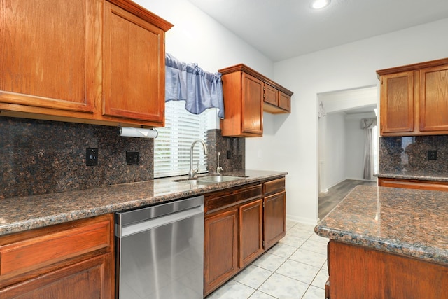 kitchen featuring dark stone counters, sink, stainless steel dishwasher, light tile patterned floors, and tasteful backsplash