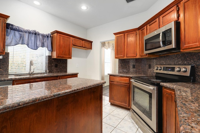 kitchen with decorative backsplash, dark stone counters, stainless steel appliances, sink, and light tile patterned floors