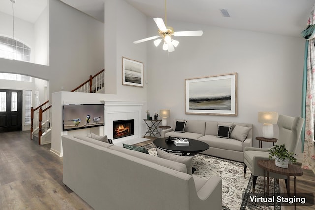 living room with hardwood / wood-style floors, ceiling fan, a tile fireplace, and high vaulted ceiling