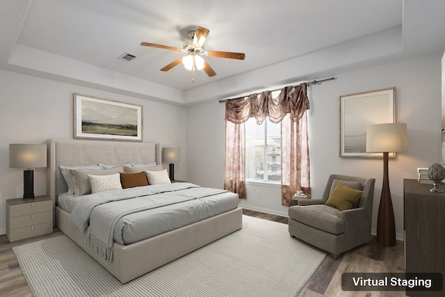 bedroom with hardwood / wood-style floors, a tray ceiling, and ceiling fan