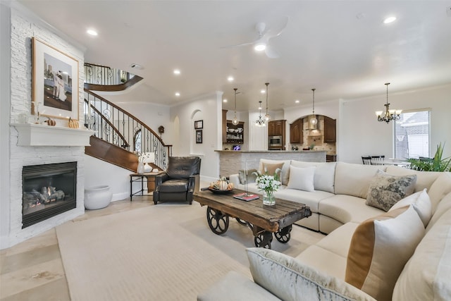 living room with ceiling fan with notable chandelier, a stone fireplace, and ornamental molding