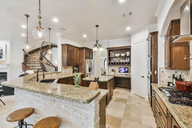 kitchen featuring a kitchen bar, stainless steel appliances, wall chimney exhaust hood, and sink