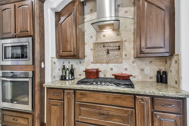 kitchen featuring light stone counters, exhaust hood, backsplash, and appliances with stainless steel finishes