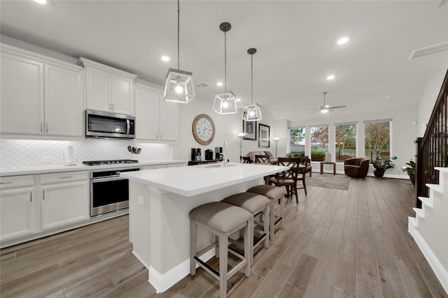 kitchen featuring white cabinetry, ceiling fan, tasteful backsplash, a kitchen island with sink, and appliances with stainless steel finishes