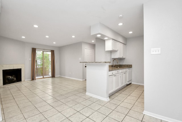 kitchen featuring light stone counters, white dishwasher, sink, a premium fireplace, and white cabinets