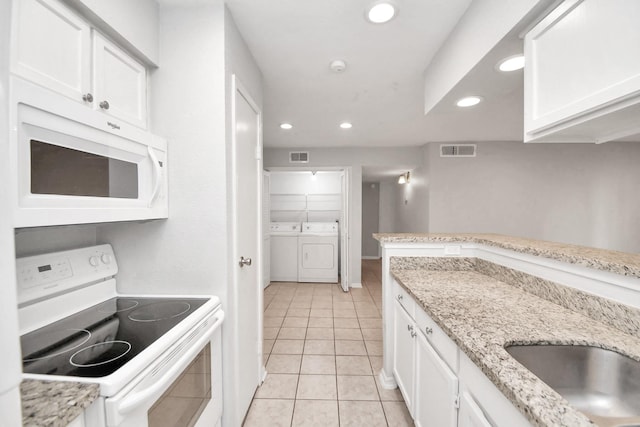 kitchen with white appliances, white cabinets, washing machine and dryer, light stone countertops, and light tile patterned floors