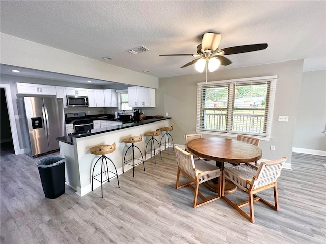 dining room with a textured ceiling, light wood-type flooring, and ceiling fan