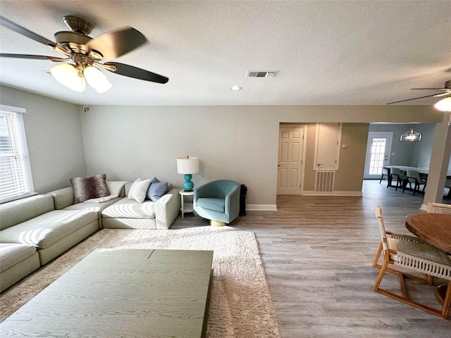 living room with plenty of natural light, ceiling fan, light wood-type flooring, and a textured ceiling