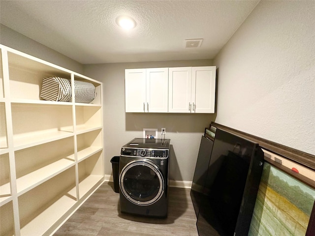 clothes washing area with cabinets, wood-type flooring, a textured ceiling, and washer / dryer