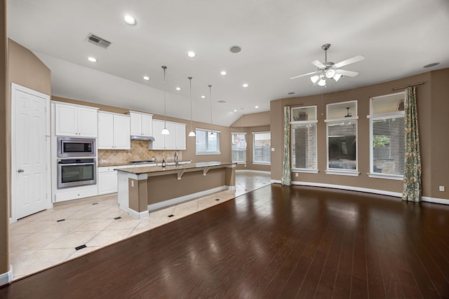 kitchen featuring pendant lighting, a kitchen breakfast bar, an island with sink, appliances with stainless steel finishes, and white cabinetry