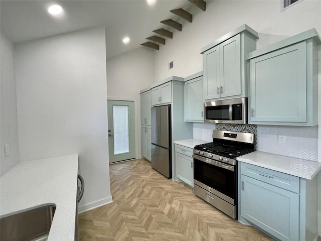 kitchen featuring beam ceiling, tasteful backsplash, high vaulted ceiling, light parquet floors, and appliances with stainless steel finishes