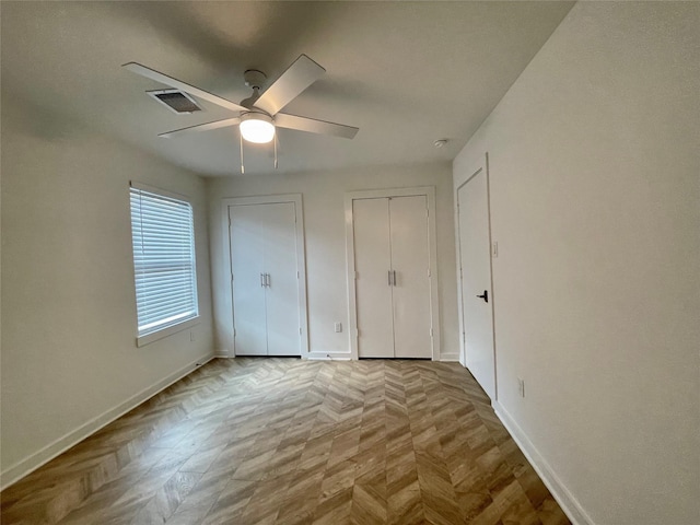 unfurnished bedroom with two closets, light parquet floors, and ceiling fan