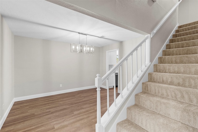 stairs featuring a notable chandelier, wood-type flooring, and a textured ceiling