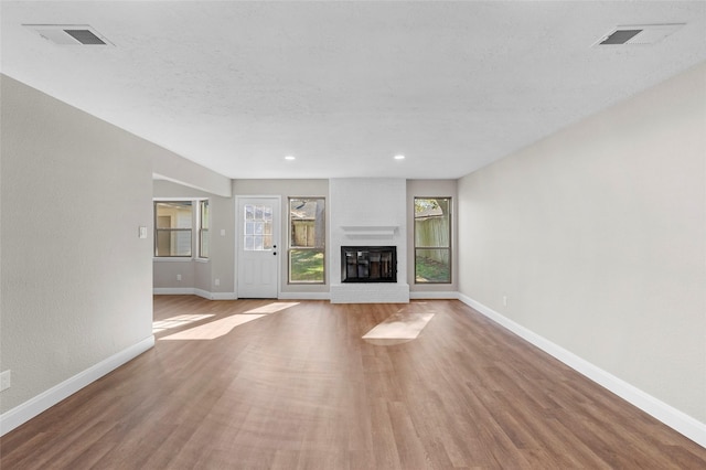 unfurnished living room with light hardwood / wood-style floors, a textured ceiling, and a brick fireplace