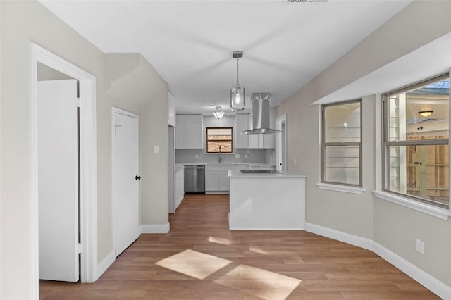 kitchen featuring hanging light fixtures, stainless steel dishwasher, hardwood / wood-style floors, island range hood, and white cabinets