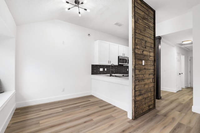 kitchen featuring lofted ceiling, white cabinets, light wood-type flooring, a textured ceiling, and tasteful backsplash