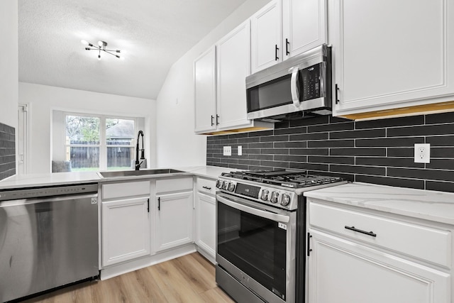 kitchen with white cabinets, sink, appliances with stainless steel finishes, and vaulted ceiling