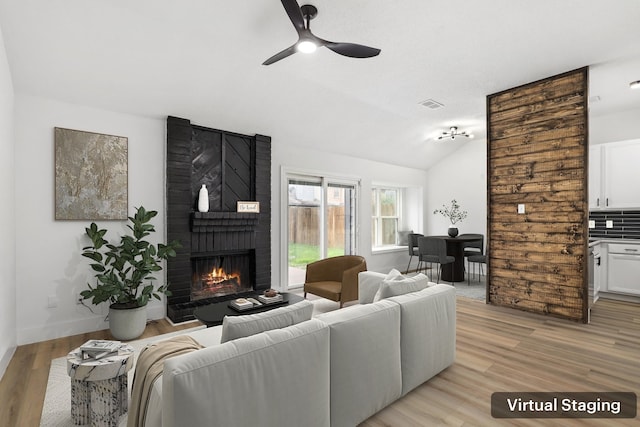 living room with a fireplace, ceiling fan, light hardwood / wood-style flooring, and vaulted ceiling