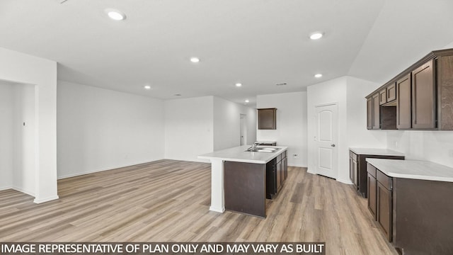 kitchen with dark brown cabinets, light wood-type flooring, a kitchen island with sink, and sink