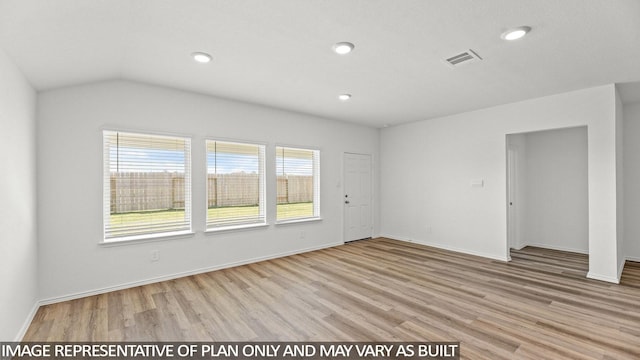 unfurnished room with a healthy amount of sunlight, vaulted ceiling, and light hardwood / wood-style floors