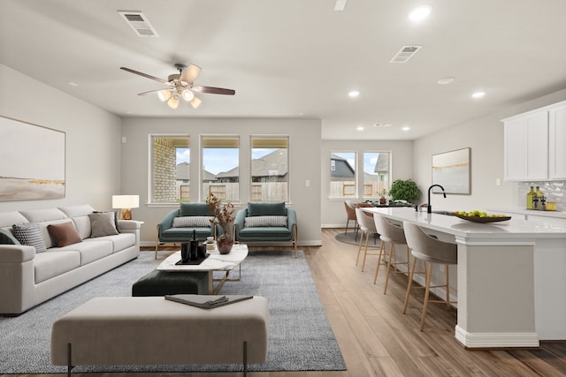 living room featuring ceiling fan, sink, and light wood-type flooring