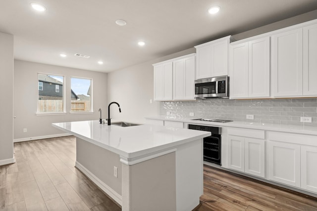 kitchen with a kitchen island with sink, sink, stovetop, white cabinets, and oven