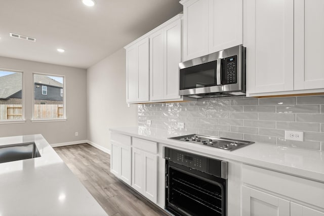 kitchen featuring white cabinetry, gas cooktop, light hardwood / wood-style flooring, black oven, and decorative backsplash