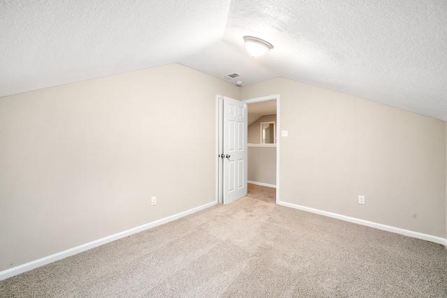 additional living space featuring lofted ceiling, a textured ceiling, and light carpet