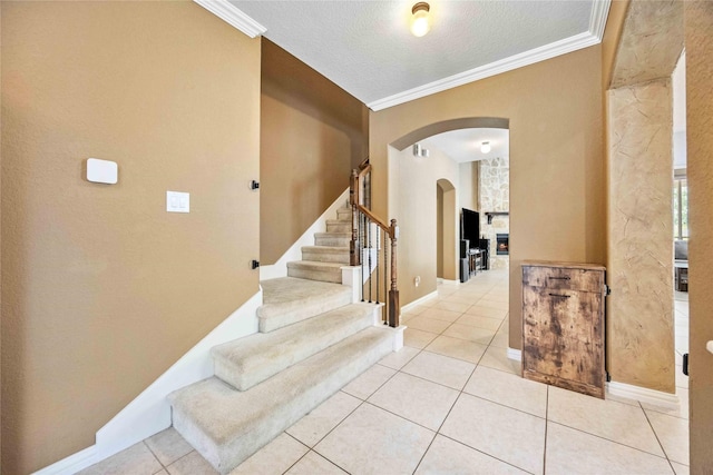 interior space with tile patterned floors, a stone fireplace, crown molding, and a textured ceiling