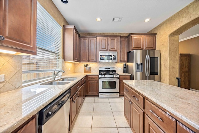 kitchen featuring backsplash, sink, light stone countertops, light tile patterned flooring, and stainless steel appliances