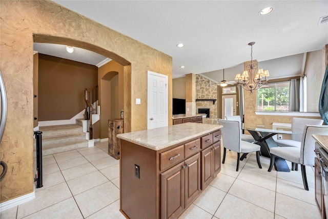 kitchen with light tile patterned floors, light stone counters, pendant lighting, a fireplace, and a kitchen island