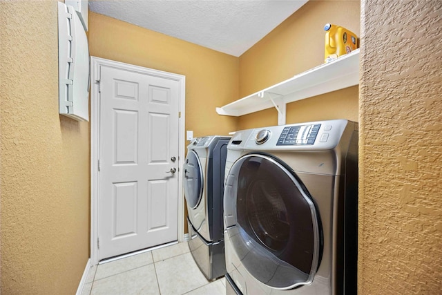 washroom featuring washer and clothes dryer, light tile patterned floors, and a textured ceiling